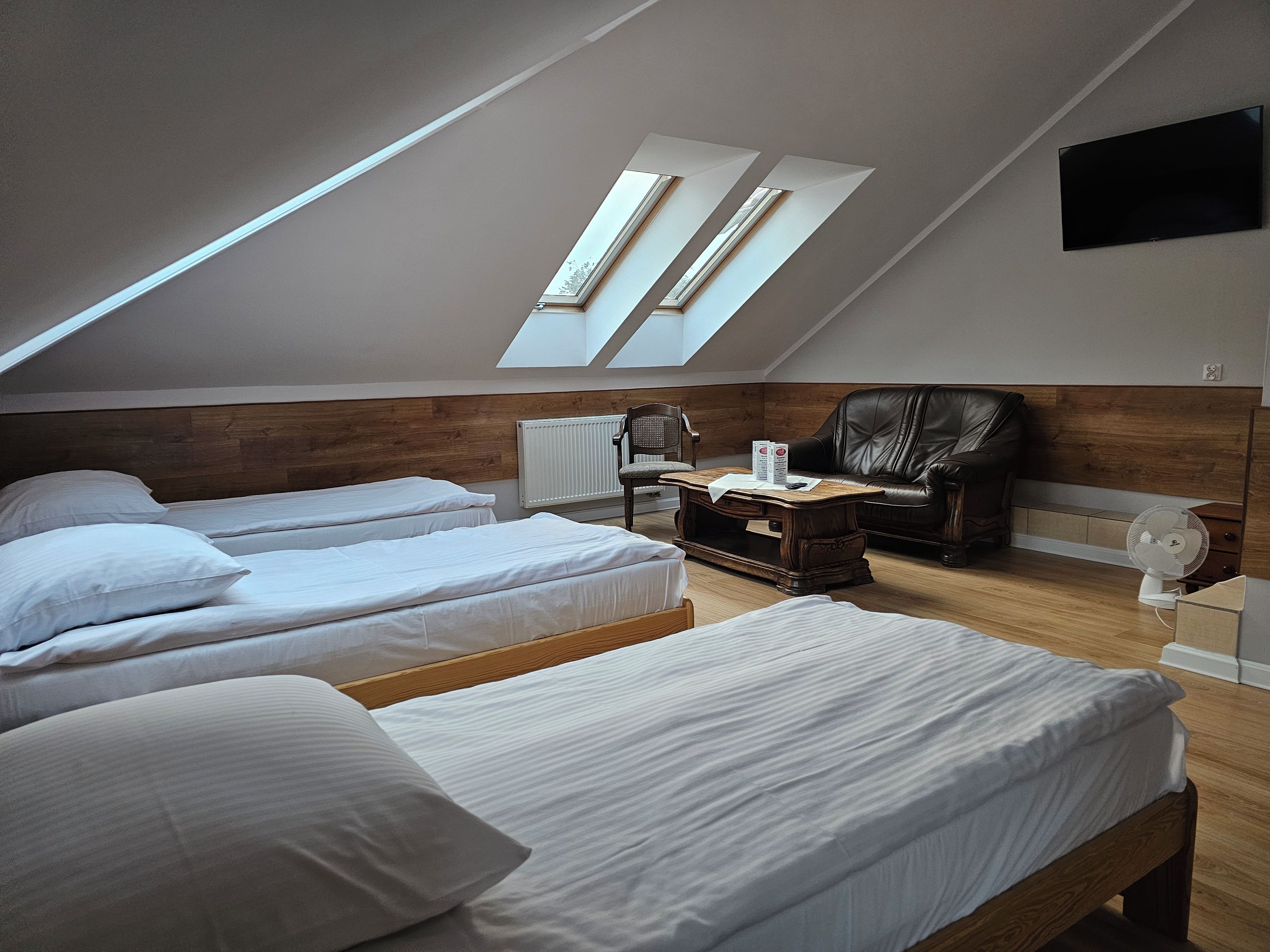 Una habitación con dos camas, un cabecero de madera, un sillón de cuero, una mesita pequeña y un tragaluz.