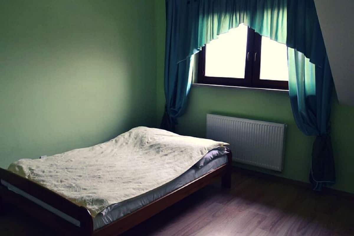 Une chambre avec un lit simple, une fenêtre avec des rideaux et un radiateur.