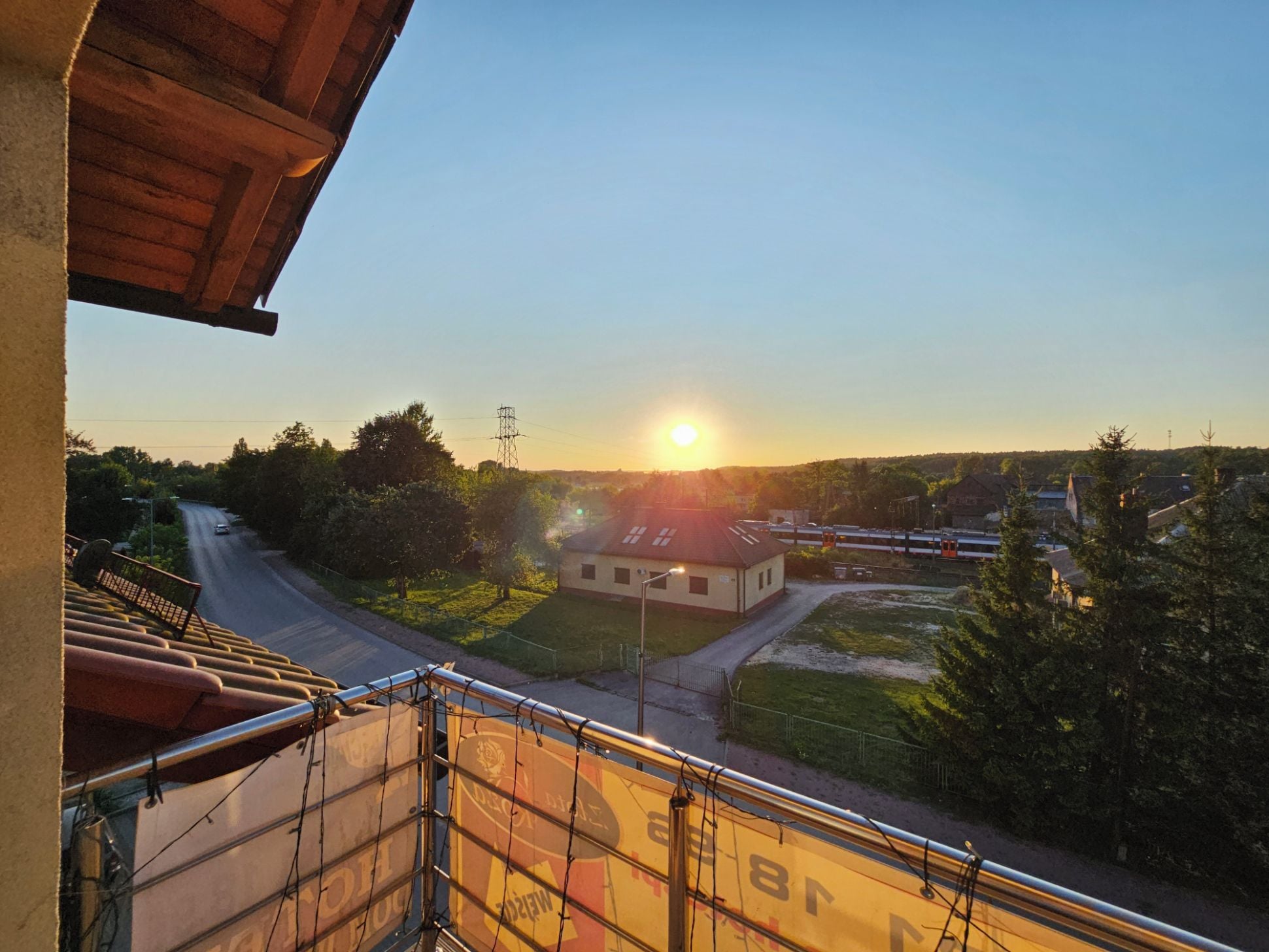 A balcony with a view of a road, a building, and a train in the distance.