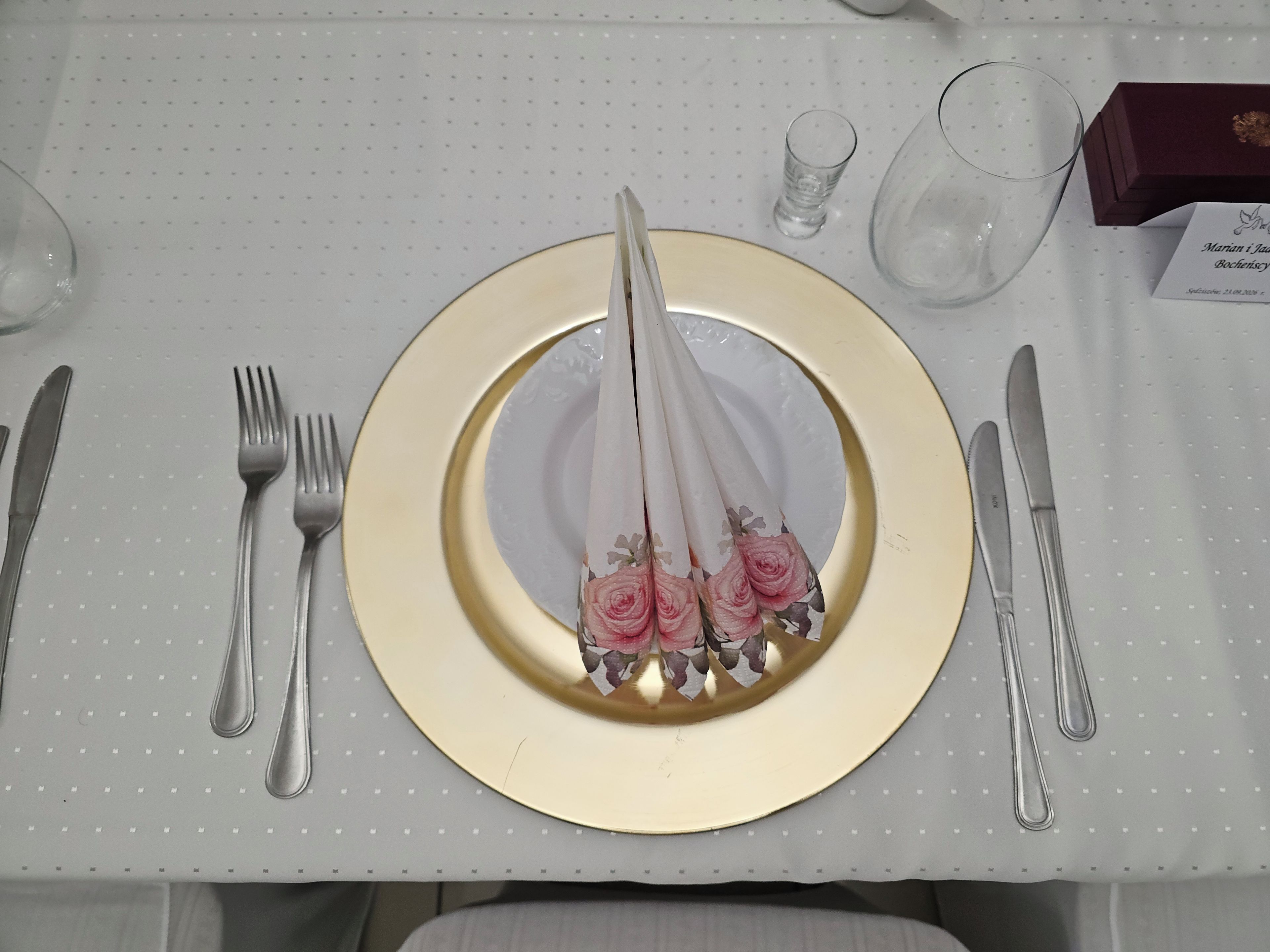 Une table dressée avec une assiette à bord doré, une serviette pliée et un verre.