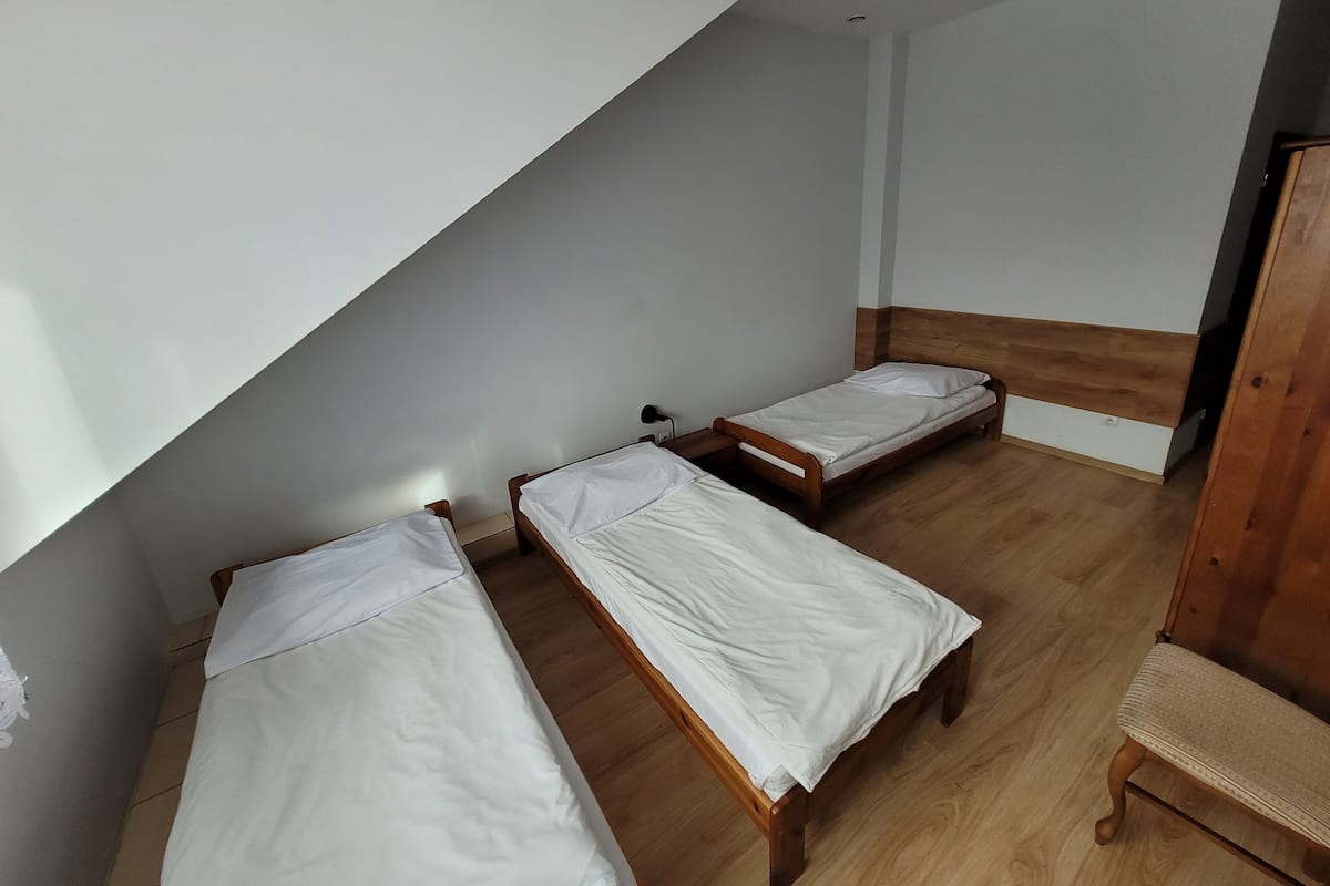 Une pièce comprenant trois lits en bois disposés dans un coin, un banc en bois et une armoire en bois.