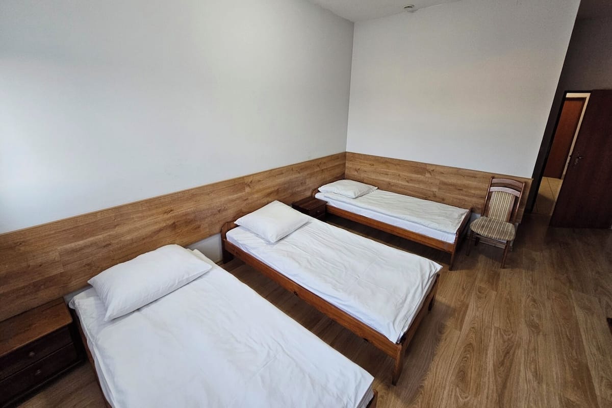 Une chambre avec trois lits en bois, chacun étant équipé de draps blancs.