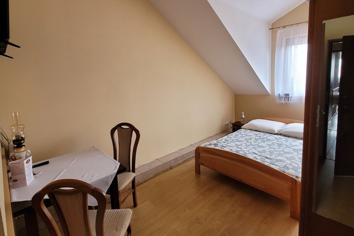 Une pièce comprenant un lit, une table, deux chaises, une lampe et une fenêtre avec des rideaux.