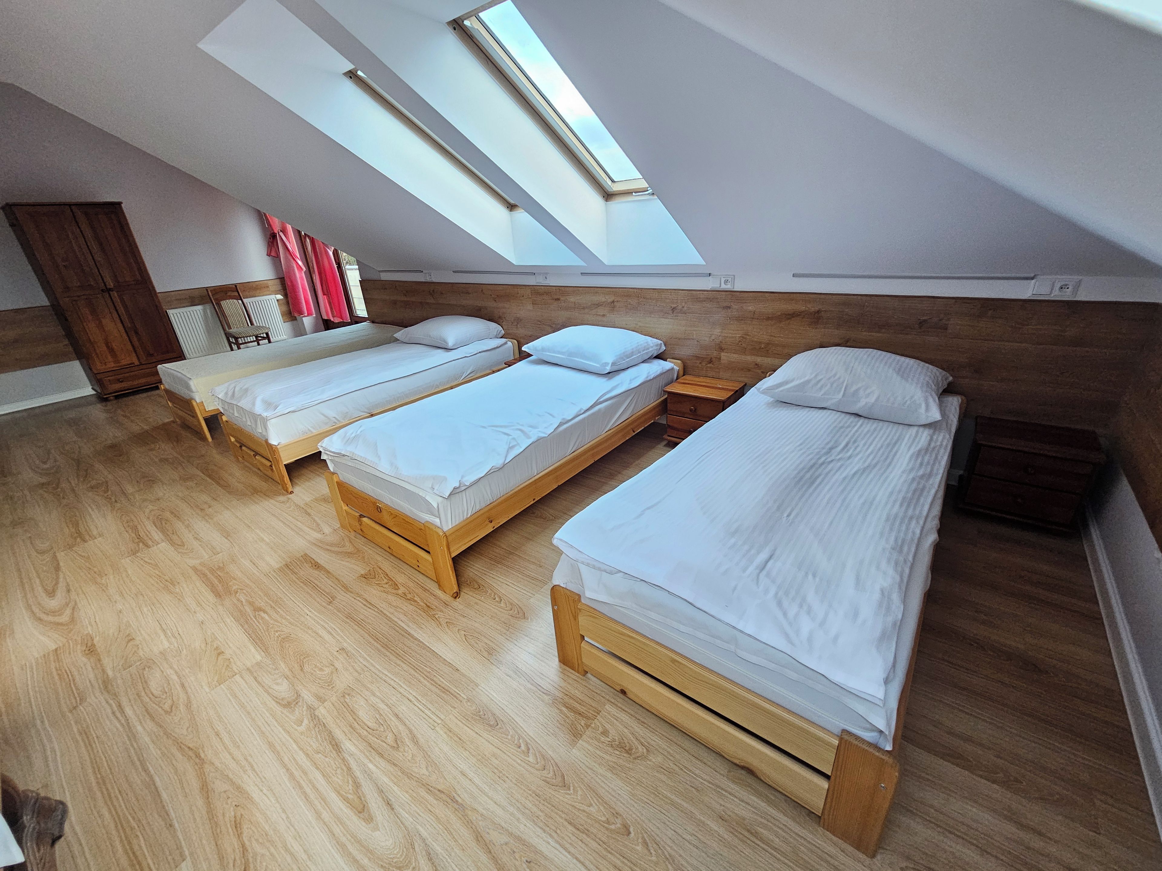 A room with three wooden beds, a wooden wardrobe, and a skylight.