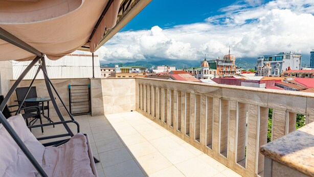 Ein Balkon mit Schaukelstuhl und Tisch, mit Blick auf eine Skyline aus Gebäuden und Bergen.