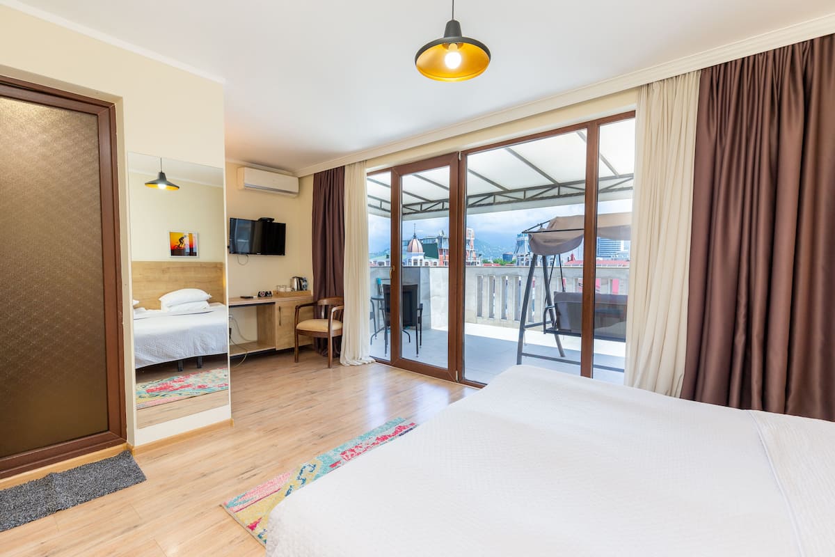 A hotel room with a bed, desk, chair, and a balcony with a view.