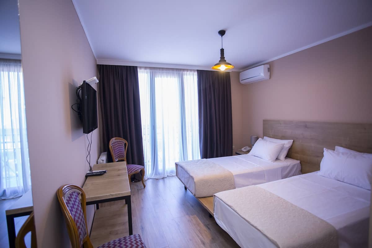 A hotel room with two beds, a desk, a chair, a TV, and a window with curtains.