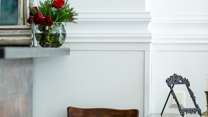 Ein Zimmer mit Holzstuhl, einer Vase mit roten Blumen und einem Spiegel an der Wand.