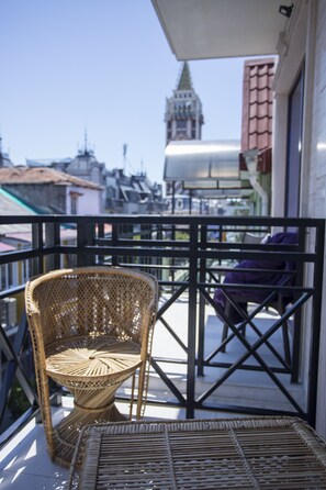A wicker chair on a balcony with a view of a building with a tower. - Hotel N16 (Batumi)