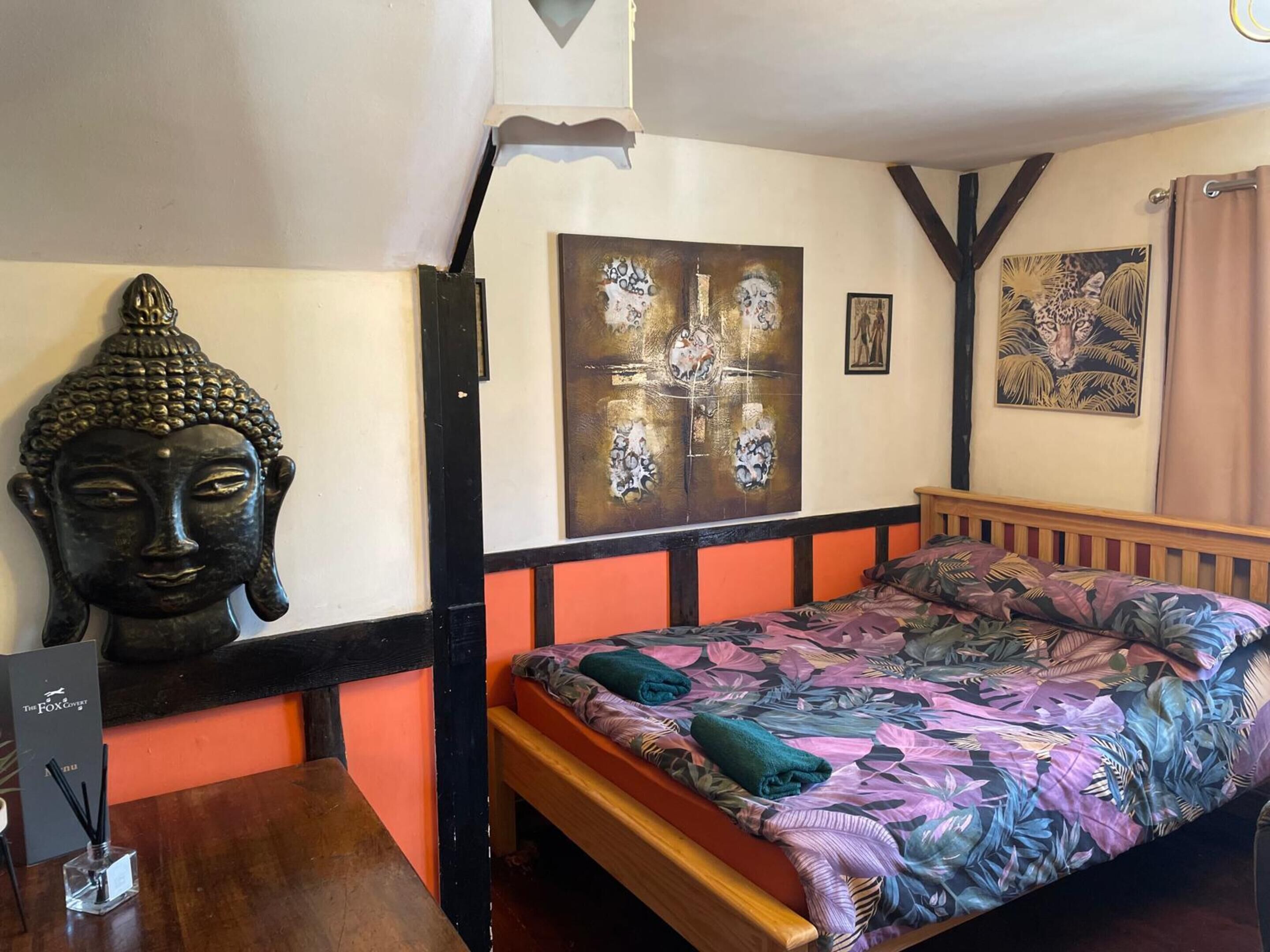 A room with a bed, a Buddha statue, and a painting on the wall.