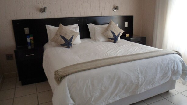A hotel room with a large bed, two nightstands, and a headboard with wall-mounted lights. - Queness Inn (Maun)