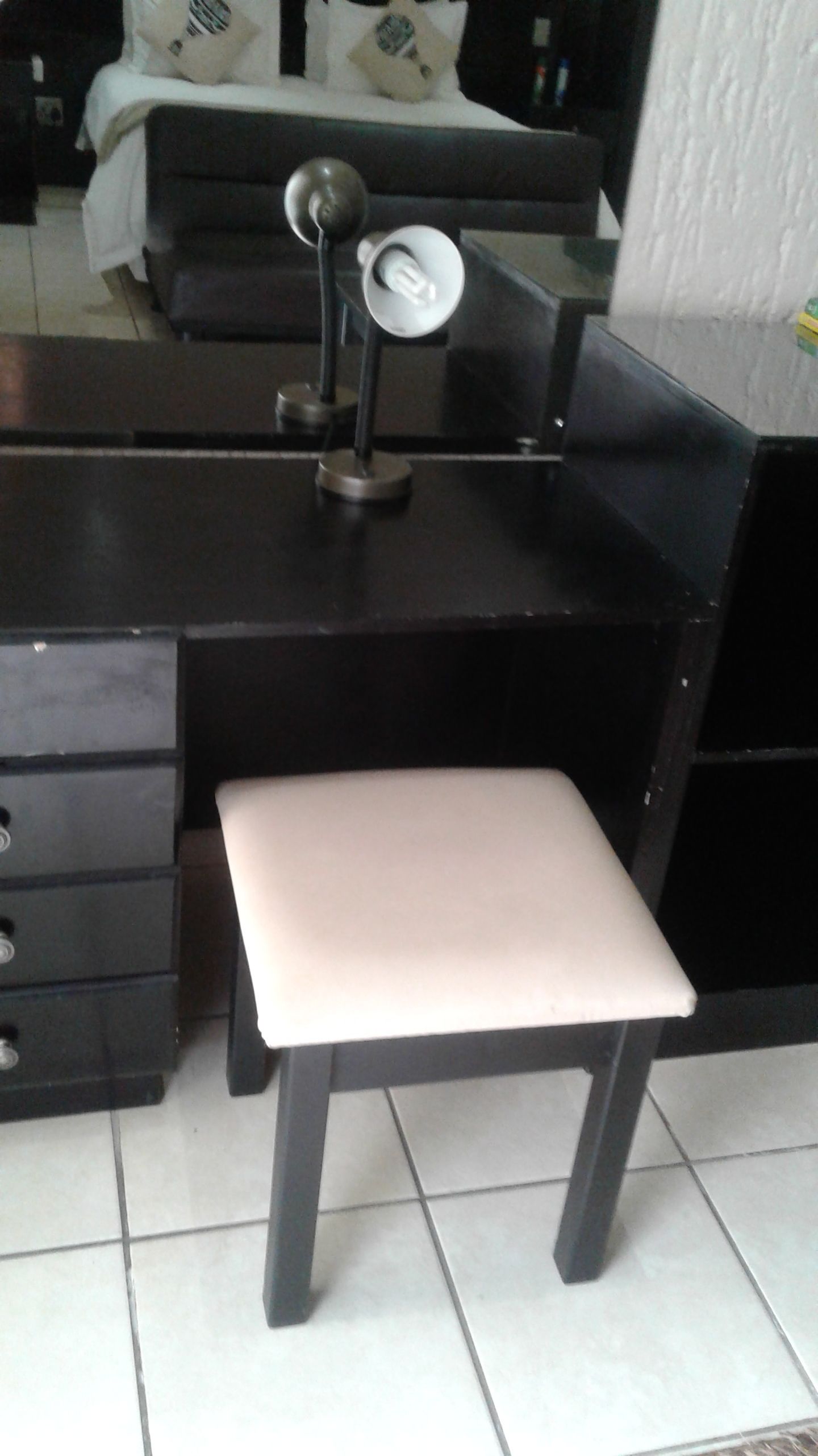 A small, dark-colored desk with a white chair, a lamp, and a drawer unit.