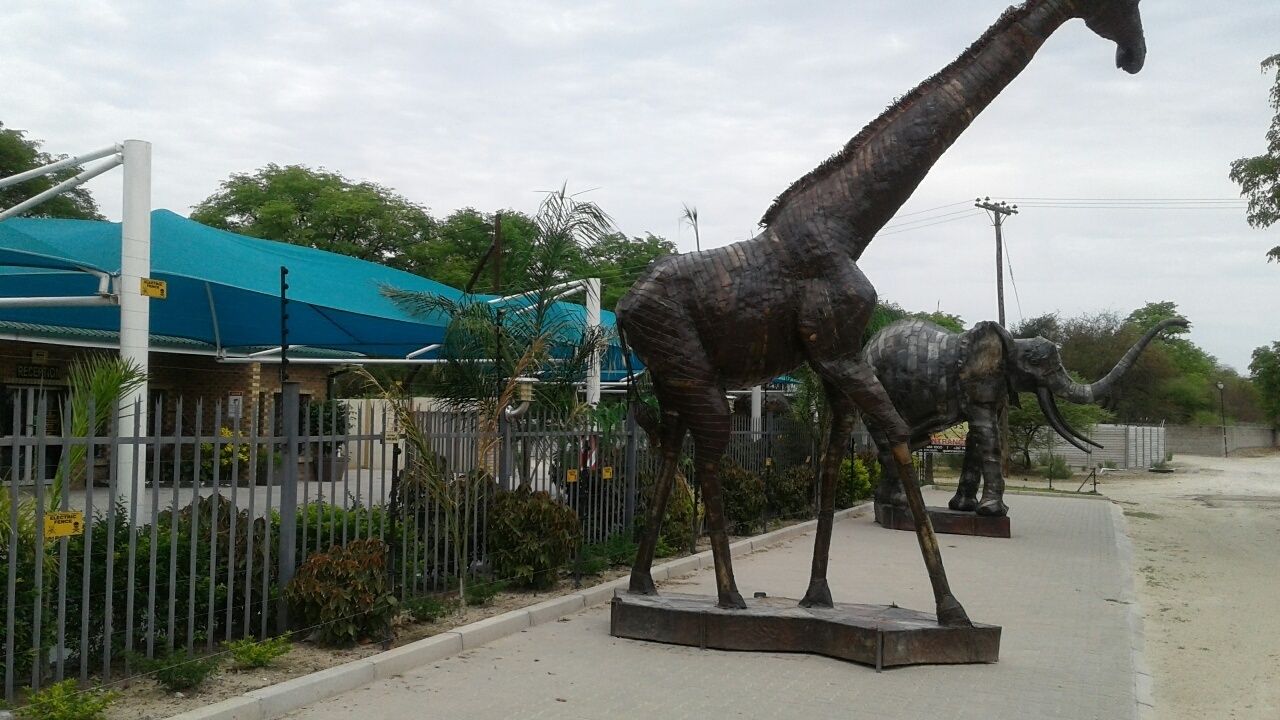 Una exhibición de dinosaurios con una estatua grande de jirafa y una estatua más pequeña de elefante.