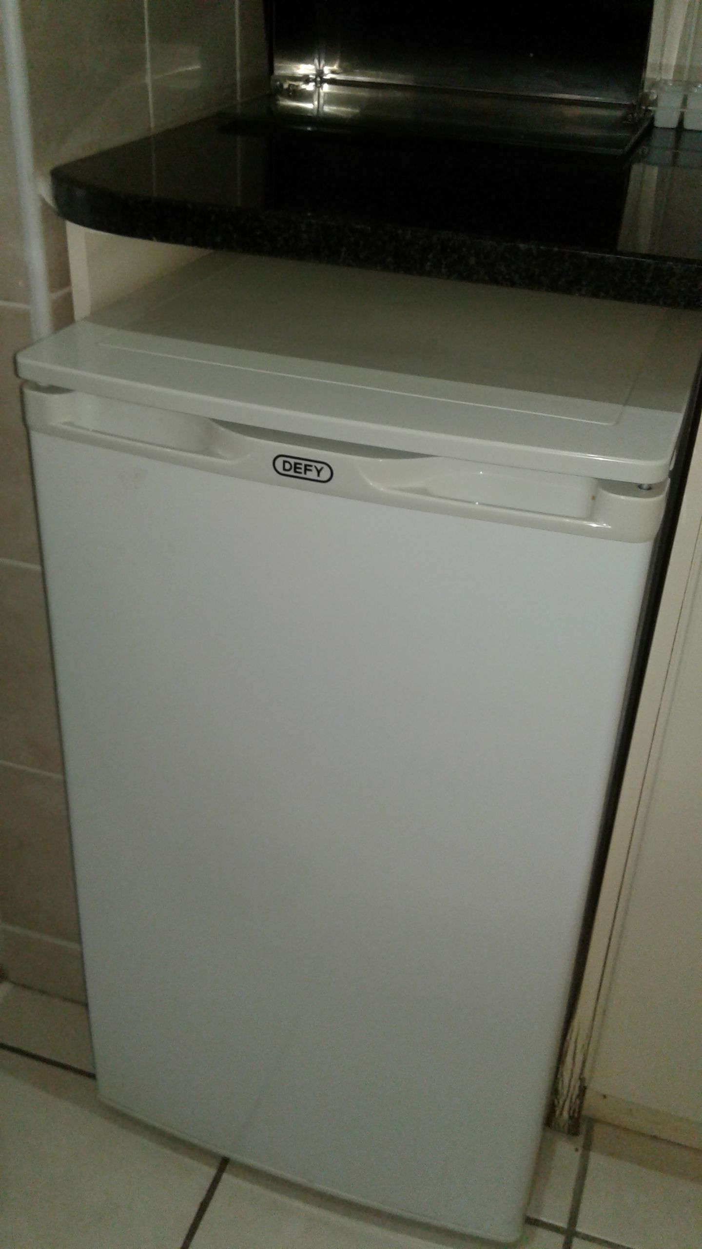 A white DEFY refrigerator in a kitchen with a black countertop above it.