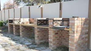A brick barbecue area with multiple grill stations, each with a metal grate and a small table. - Queness Inn (Maun)