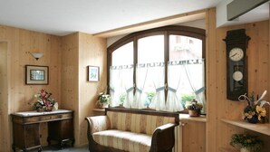 A cozy room with a wooden bench, a wooden cabinet, and a large window with curtains. - Hotel Compagnoni (Valfurva)