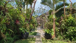 Un sentier bordé de plantes luxuriantes mène à un espace de détente abrité, entouré d’une végétation abondante et de grands pots de fleurs.