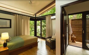 A bedroom with a bed, a nightstand with a lamp, a window with curtains, and a view of greenery outside. - Isla Palenque Member of the Cayuga Collection (Boca Chica)