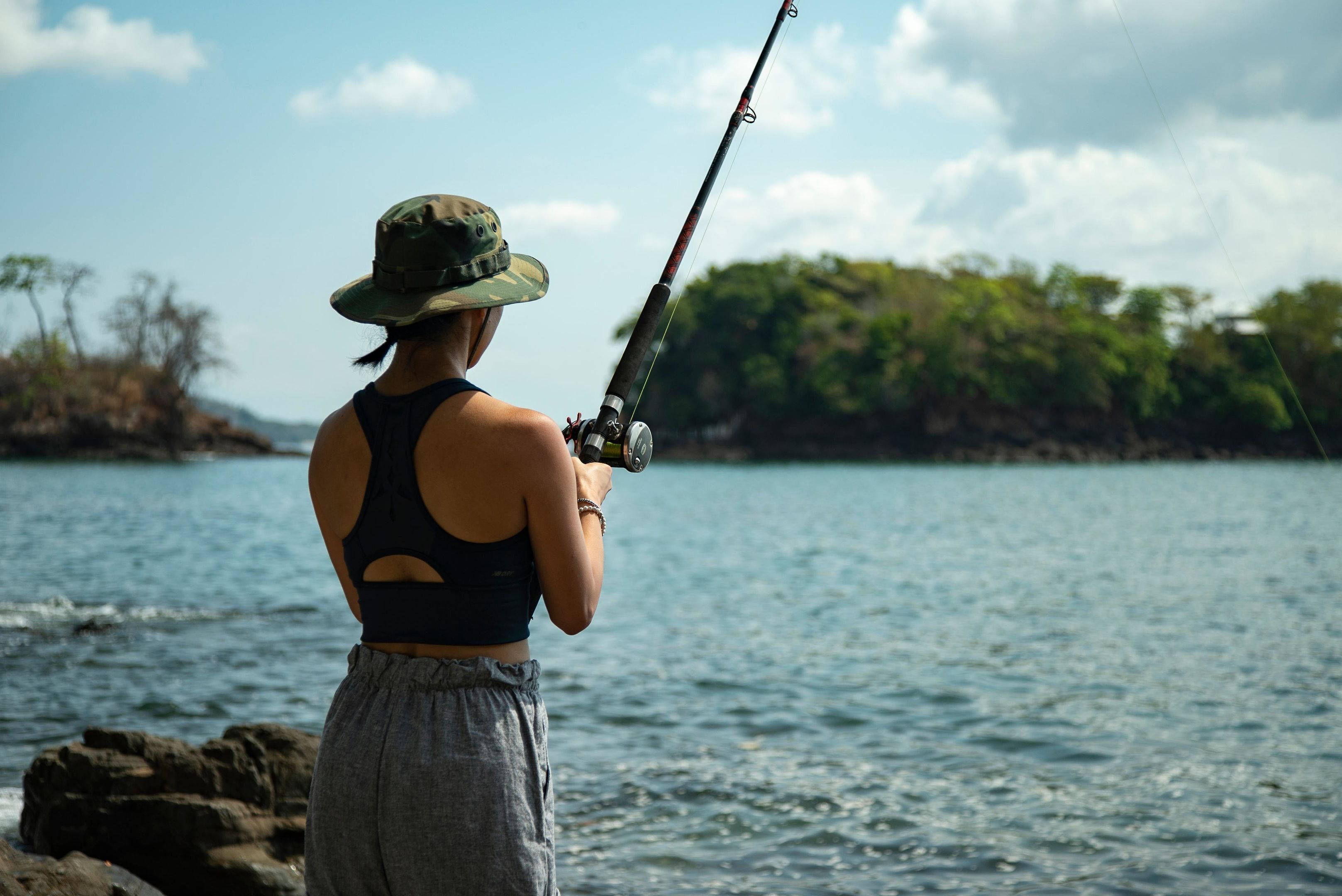 A person fishing by a body of water with a clear sky.