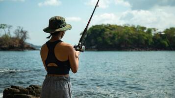 A person fishing by a body of water with a clear sky.