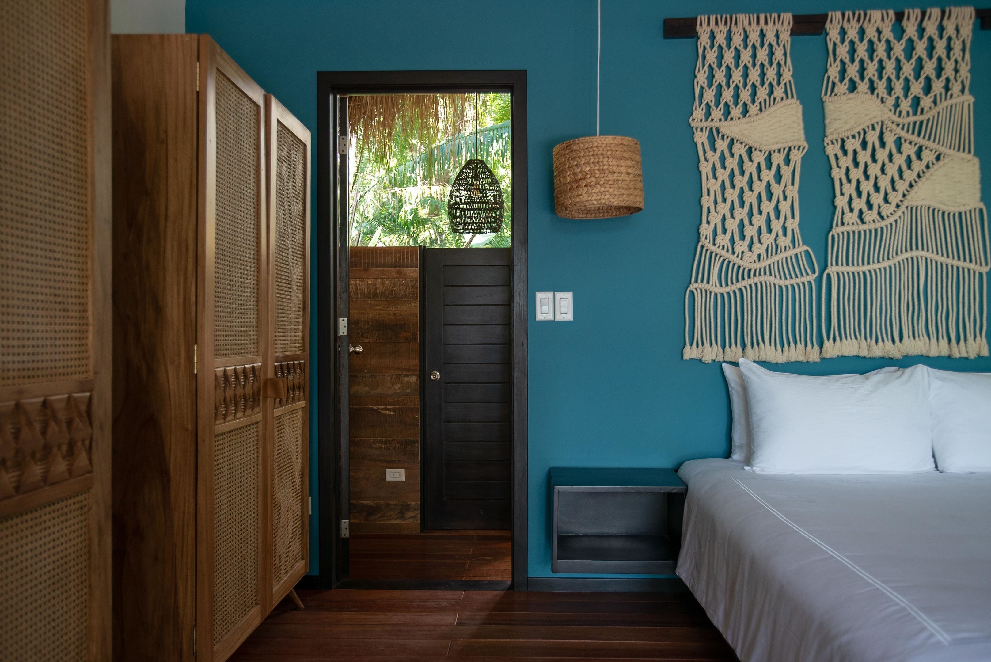 A room with a bed, a door leading outside, and a macrame wall hanging.