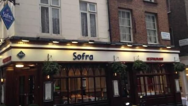 Un bâtiment dont le rez-de-chaussée porte une enseigne indiquant « Sofra », ce qui laisse supposer qu’il s’agit d’un restaurant ou d’un café.