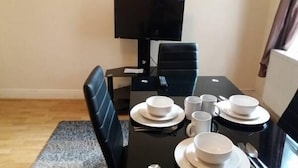Un coin repas avec une table noire dressée pour quatre personnes, comprenant des assiettes, des bols et des tasses.