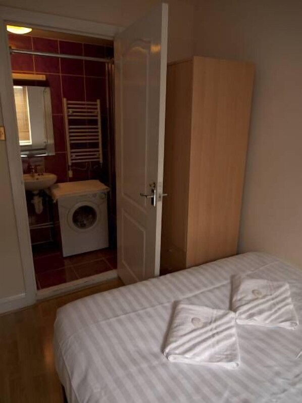 A bedroom with a bed, a wardrobe, a washing machine, and a bathroom visible through an open door. - Mayfair Apartment (London)