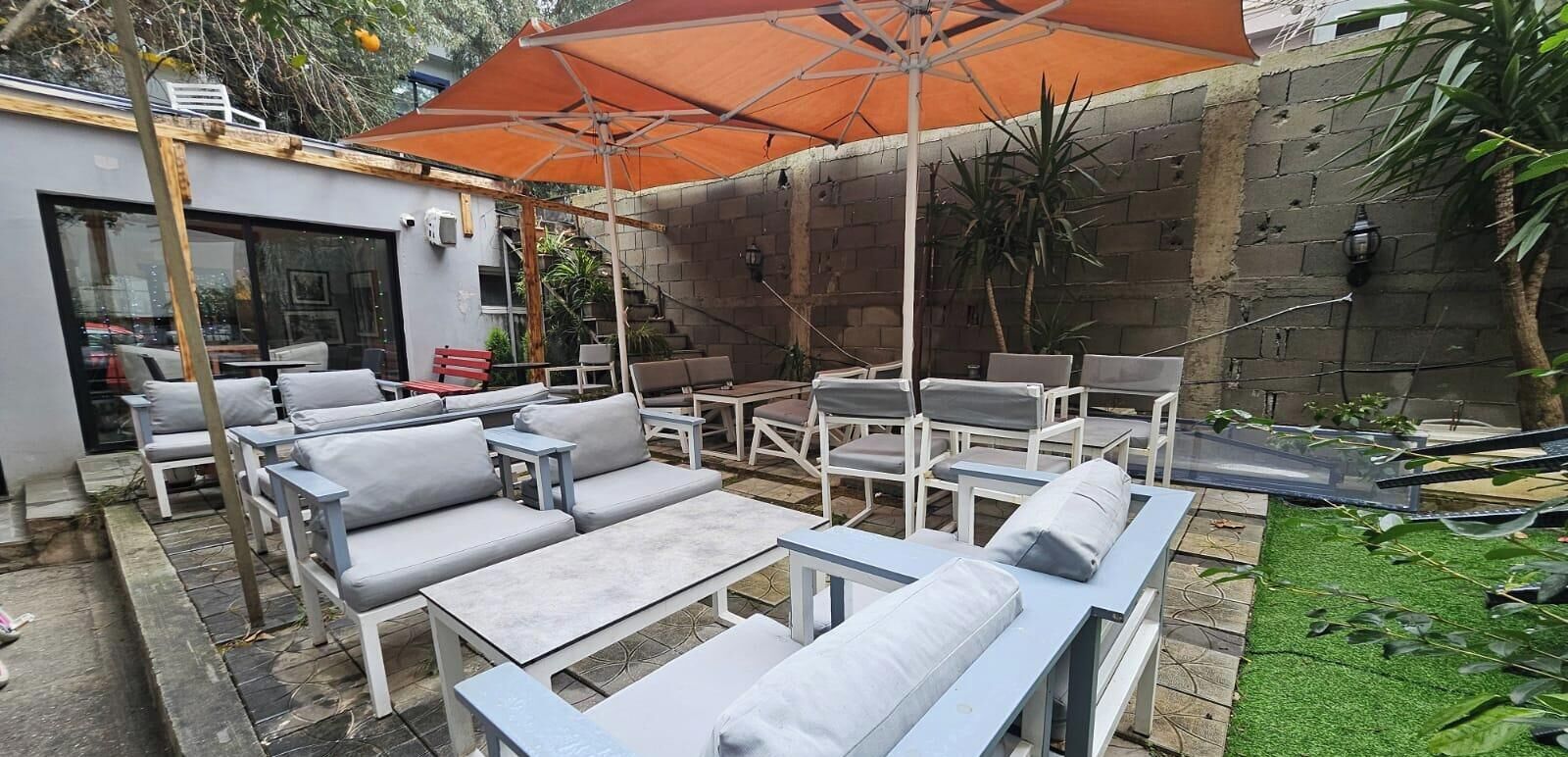 An outdoor patio with grey and white furniture, including sofas, chairs, and tables, under a large orange umbrella.