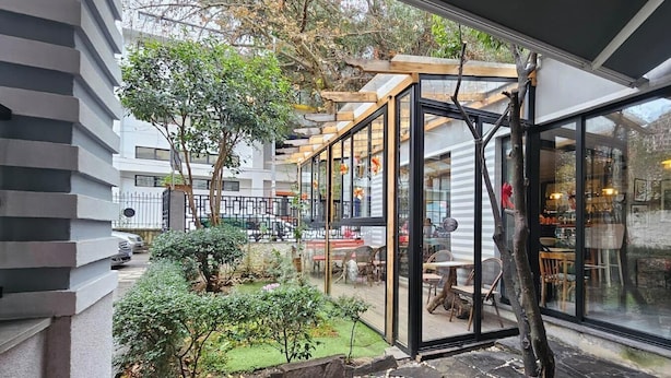 A modern building with a glass facade, outdoor seating area, and a garden. - Hotel Antigone (Tirana)