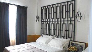 A neatly made bed with white bedding, a geometric wall panel, and a small table with a vase of flowers. - Hotel Antigone (Tirana)