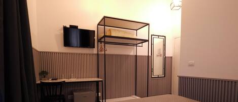 A bedroom with a bed, a desk, a chair, a TV, and a radiator.