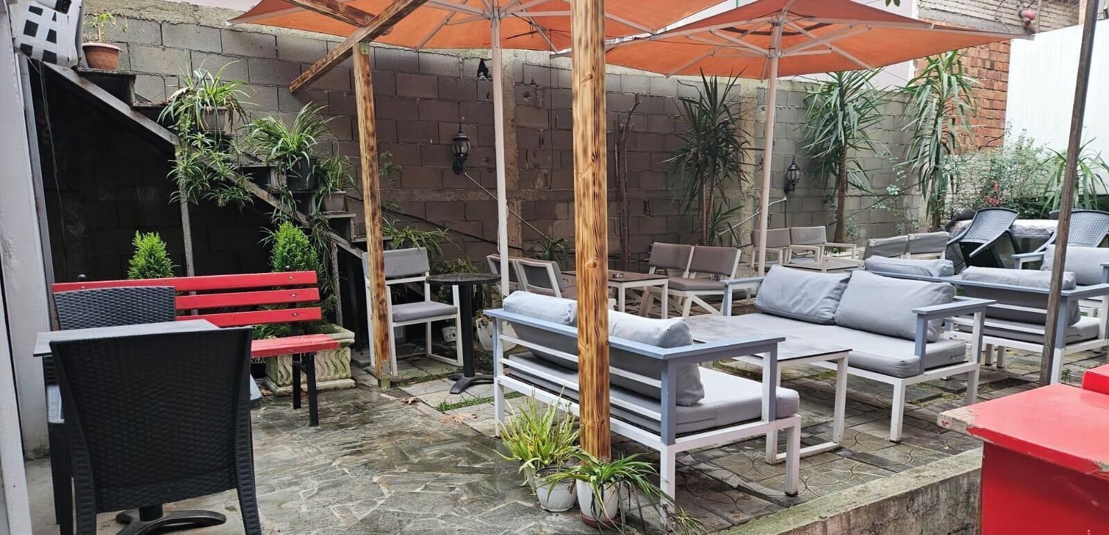 Patio esterno con pavimento in pietra, una panca rossa e diverse opzioni di seduta, tra cui divani e poltrone.