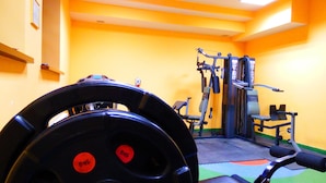 Un gimnasio con equipo de levantamiento de pesas, incluyendo barra y discos, y una banca.