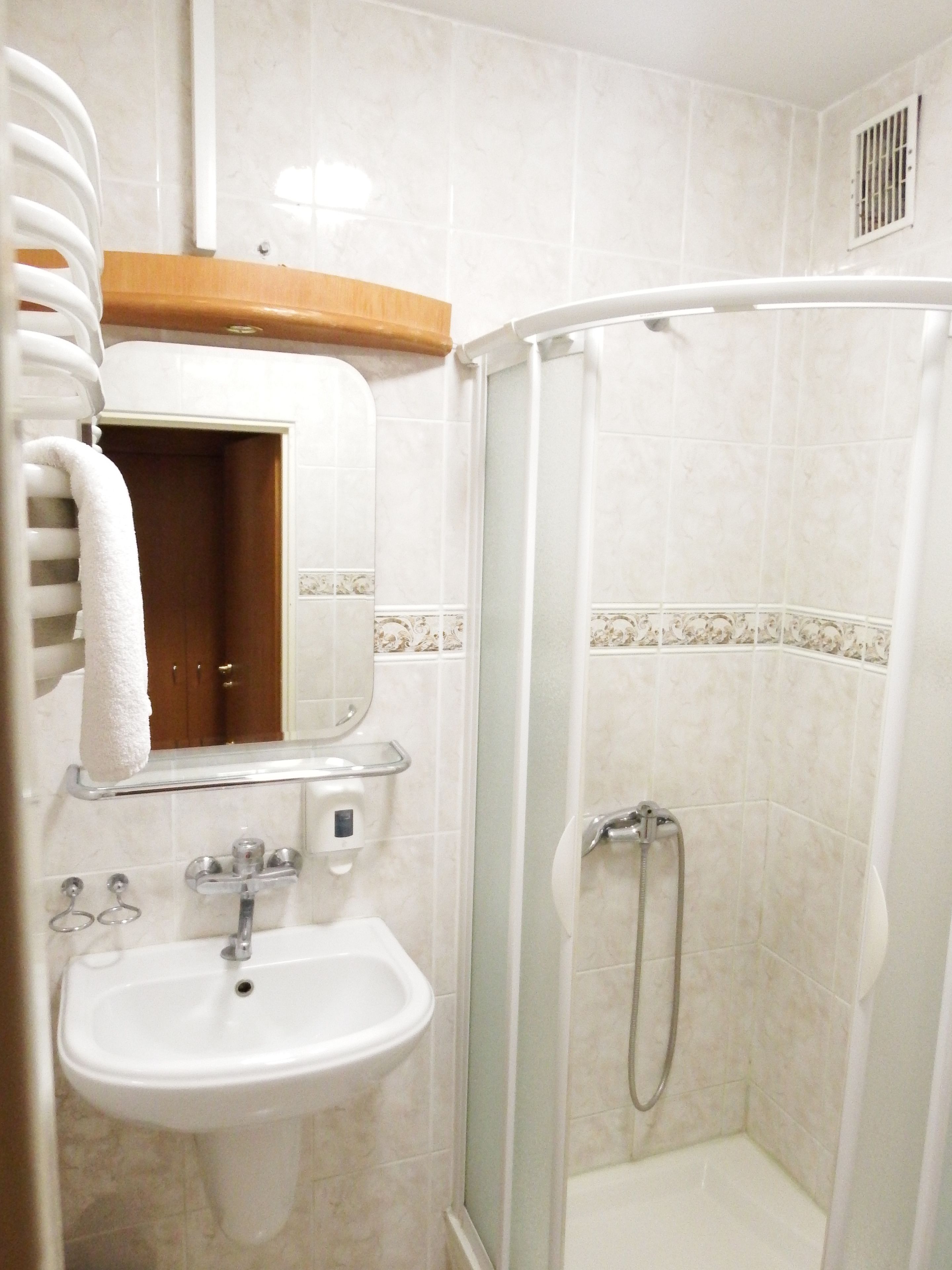 A bathroom with a sink, mirror, towel rack, shower, and a wooden shelf.