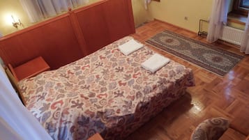 Camera da letto con testiera in legno, copripiumino decorato, due asciugamani sul letto, pavimento in legno, tappeto e finestra con tende.