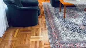Una sala de estar con escalera de madera, sofás de cuero negro, una mesa de centro de madera y una alfombra estampada.