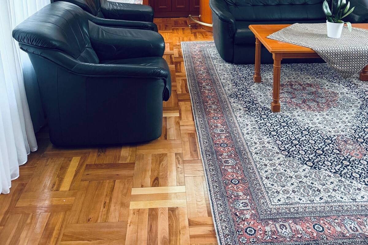 Una sala de estar con escalera de madera, sofás de cuero negro, una mesa de centro de madera y una alfombra estampada.