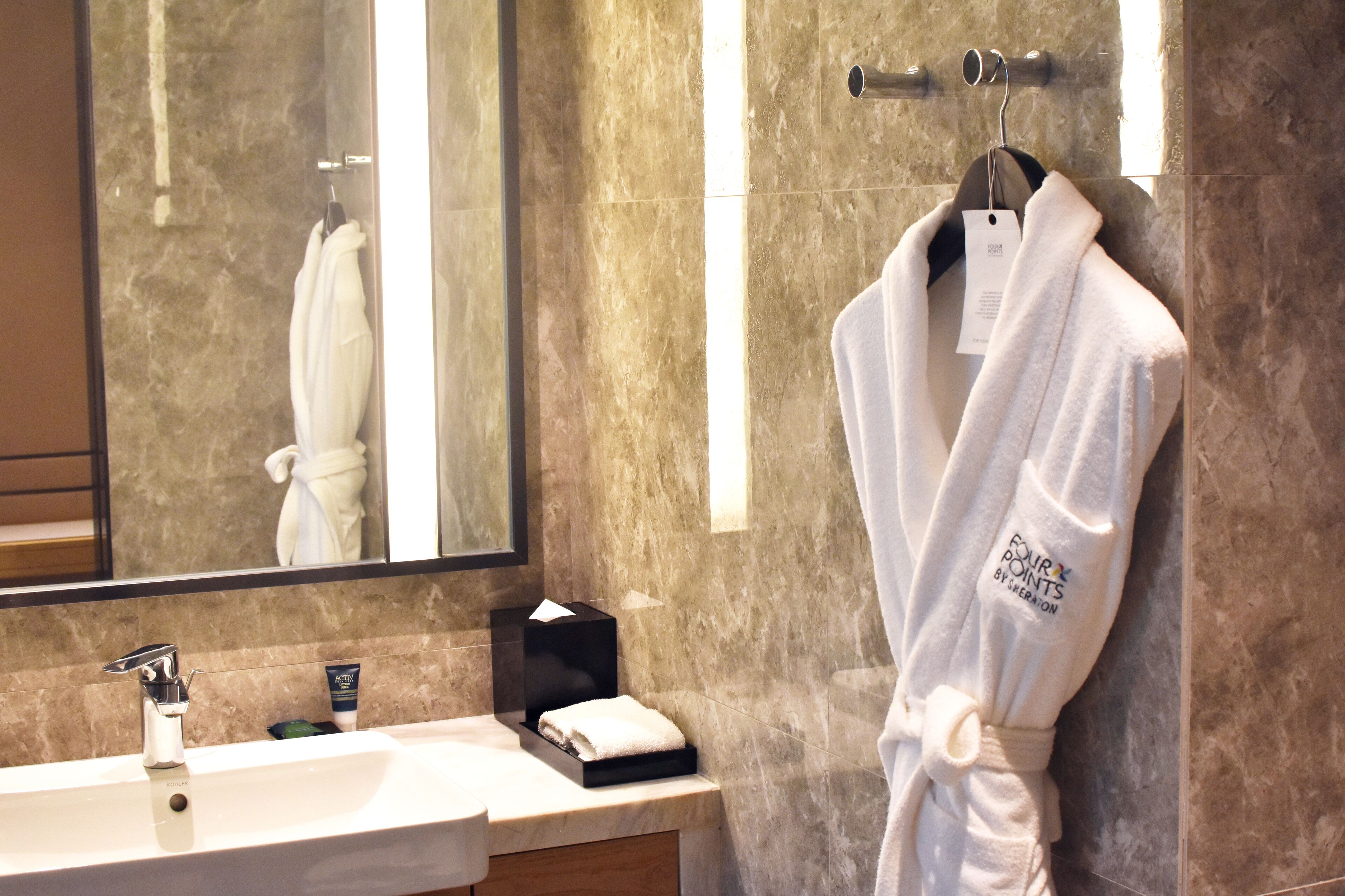 Un bagno con parete in marmo, un lavandino con asciugamano e una vestaglia appesa a un appendiabiti.