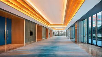 Un couloir d’hôtel moderne, doté d’un long plancher poli, de murs recouverts de panneaux en bois et d’un plafond pourvu d’un éclairage linéaire.