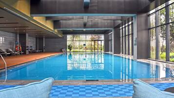 An indoor swimming pool with clear blue water, surrounded by large windows and a tiled floor.