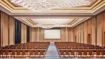 Un salón de conferencias con filas de sillas, una pantalla grande y un diseño de techo moderno.