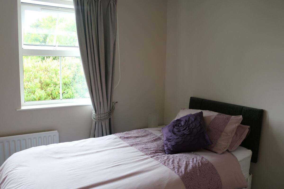 A bedroom with a bed, a window with curtains, and a view of greenery outside.