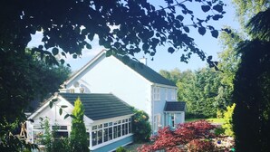 A white house with a large glass conservatory, surrounded by a well-maintained garden with various plants and a gravel path. - Five Oaks Bed & Breakfast (Londonderry)