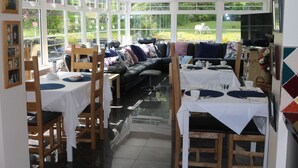 A dining area with a glass partition, wooden chairs, a black sofa, and a table set for a meal. - Five Oaks Bed & Breakfast (Londonderry)