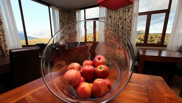 A dining table with a glass bowl containing apples, a wooden chair, and a view of a desert landscape through large windows. - La Senda de los Enebros (Higuera de las Duenas)