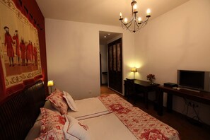A hotel room with a large bed, a desk with a TV, a chandelier, and a painting on the wall. - La Senda de los Enebros (Higuera de las Duenas)