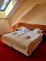 Quarto de hotel com cama, mesa de cabeceira, luminária e claraboia.