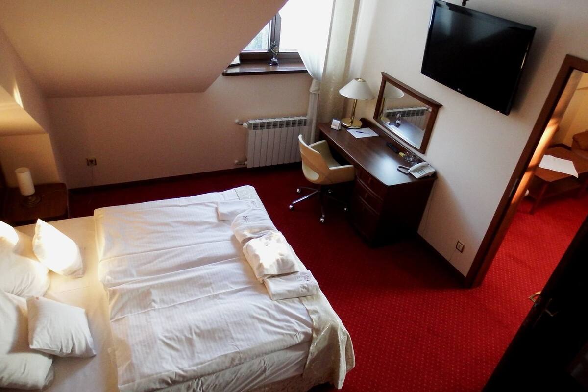 A hotel room with a large bed, a desk with a chair, a flat-screen TV, and a window.