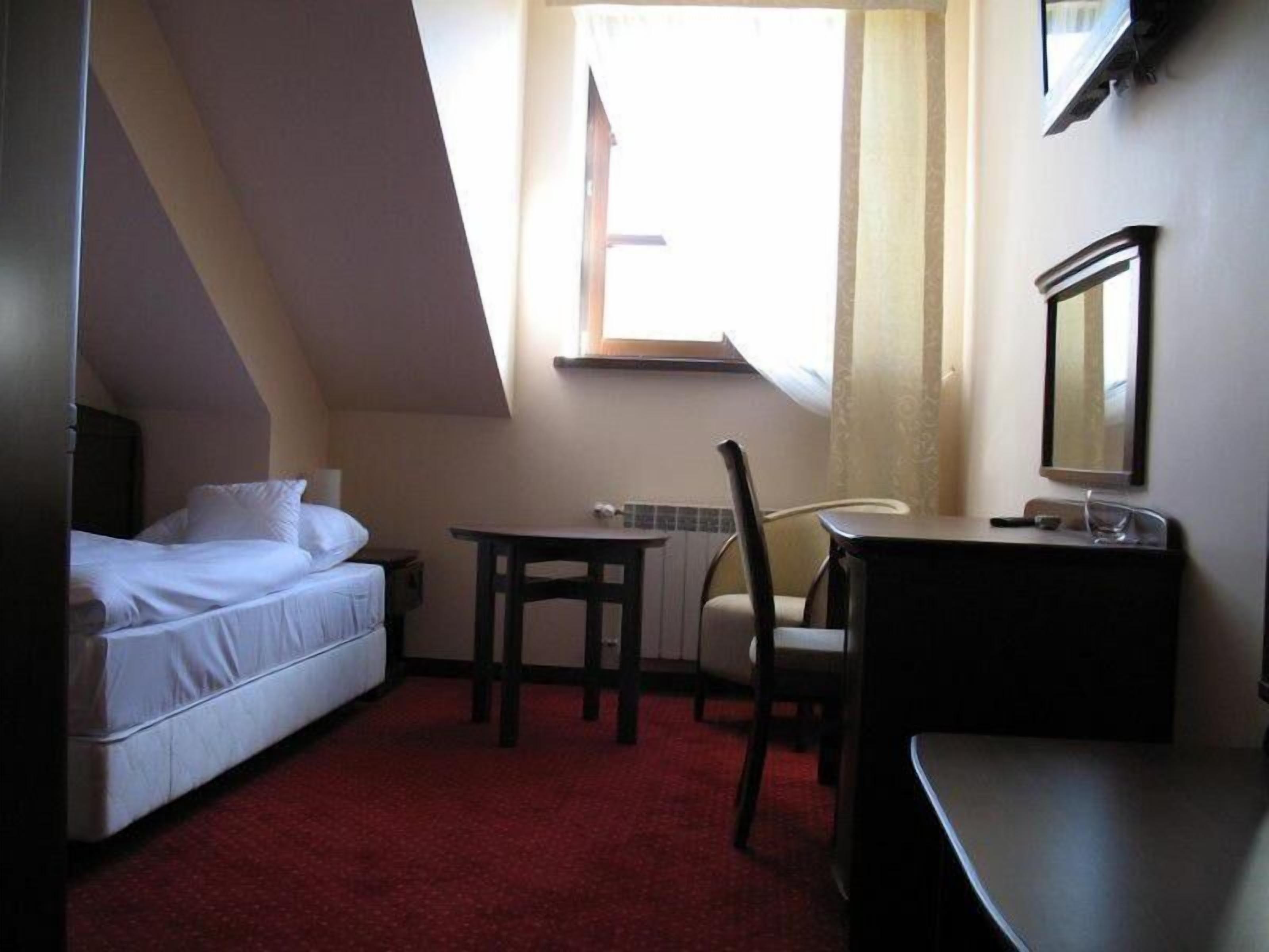 A small, compact room with a bed, a desk, a chair, and a dresser. There is a window providing natural light.